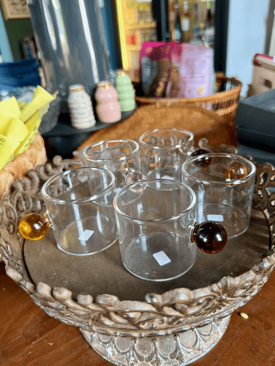 17 Fall-Ready Nashville FINDS: Cozy Layers, Beauty & Spooky Season Style - 14 Six small glass cups with round, colored handles are arranged on a decorative tray—a charming example of Nashville finds October. Some cups have white price stickers.