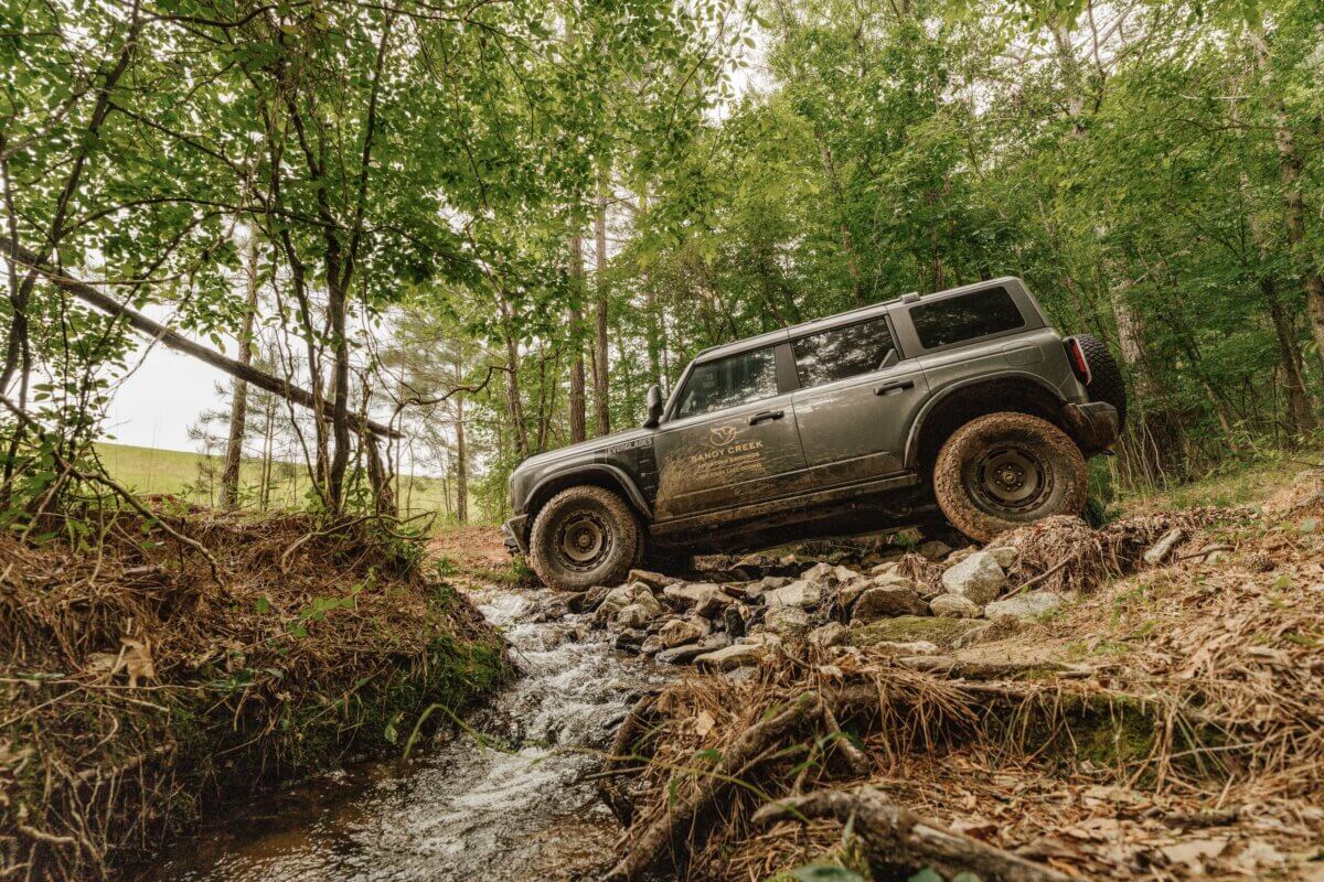 Lake Oconee: Your Guide to a Luxe Georgia Getaway - 4 A black SUV with muddy tires is crossing a shallow rocky creek in a forested area near Lake Oconee during the day, offering a glimpse of the adventurous side of Greensboro GA.