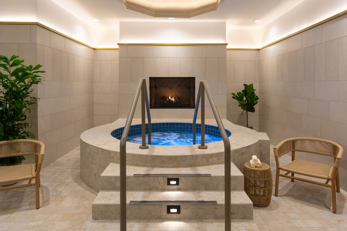Lake Oconee: Your Guide to a Luxe Georgia Getaway - 5 A round indoor hot tub with bubbling water awaits you in this serene Greensboro GA retreat, featuring steps leading up, two chairs, potted plants, and a lit fireplace on the far wall—the perfect setting for your Lake Oconee weekend experience.