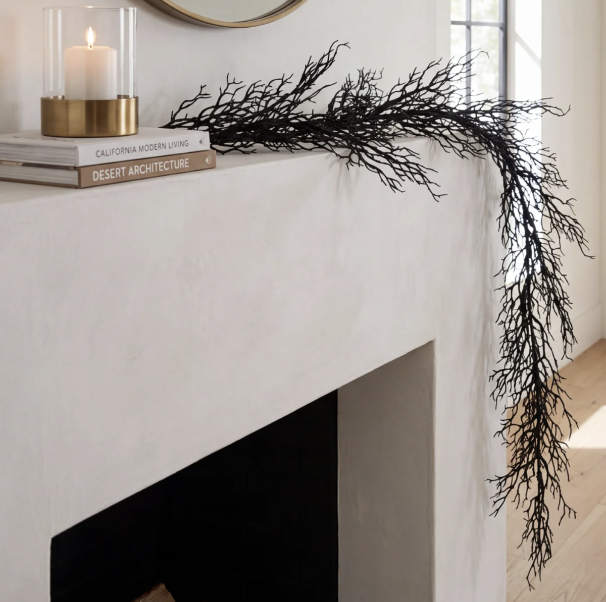 20 Halloween Decor FINDS That Are Actually Chic - 6 A white mantel with two books, a glass candle holder, and a long black decorative branch draped over the edge; sunlight streams in from a nearby window, casting just the right mood for some subtle Halloween decor.