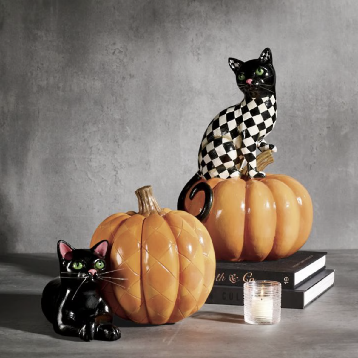20 Halloween Decor FINDS That Are Actually Chic - 11 Two ceramic black cats with green eyes, one sitting on a pumpkin and one perched on books beside a pumpkin, with a small lit candle in front—a charming touch of Halloween Decor perfect for spooky season.