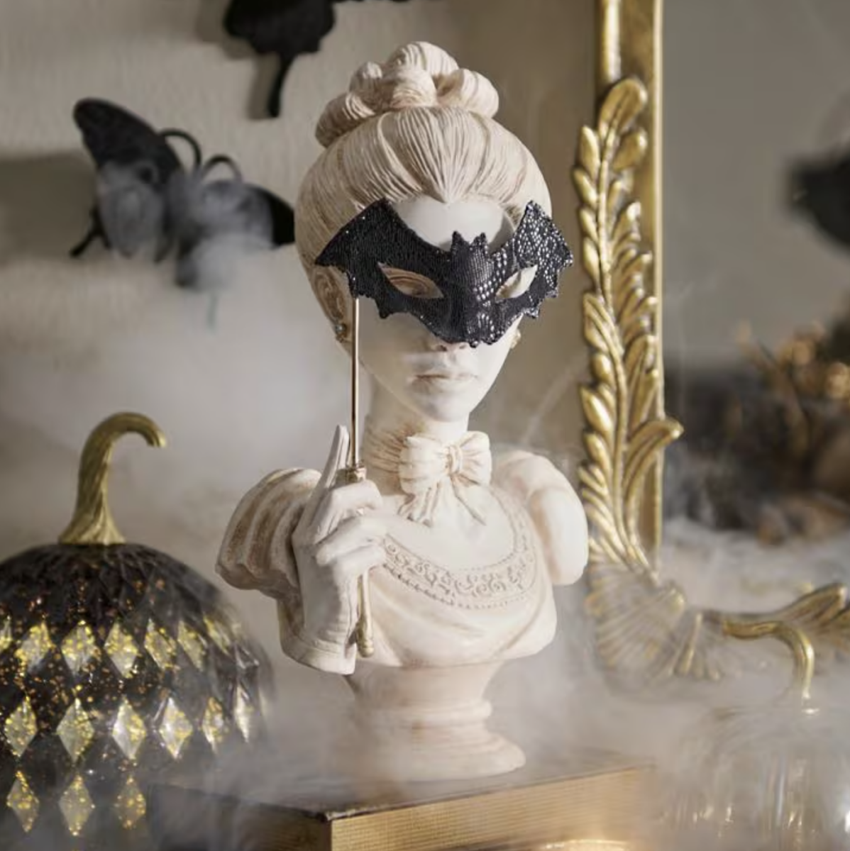 20 Halloween Decor FINDS That Are Actually Chic - 12 Bust of a woman in a Victorian-style dress holding a black masquerade mask, surrounded by fog, with a gold and black pumpkin and ornate mirror in the background—perfect Halloween Decor for those seeking unique Halloween Finds this Spooky Season.