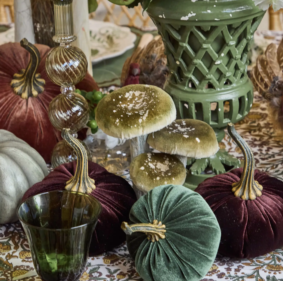 20 Halloween Decor FINDS That Are Actually Chic - 21 Velvet pumpkins and faux mushrooms are arranged on a patterned tablecloth with glass decor and a green lattice vase in the background, creating the perfect blend of Halloween decor for spooky season.
