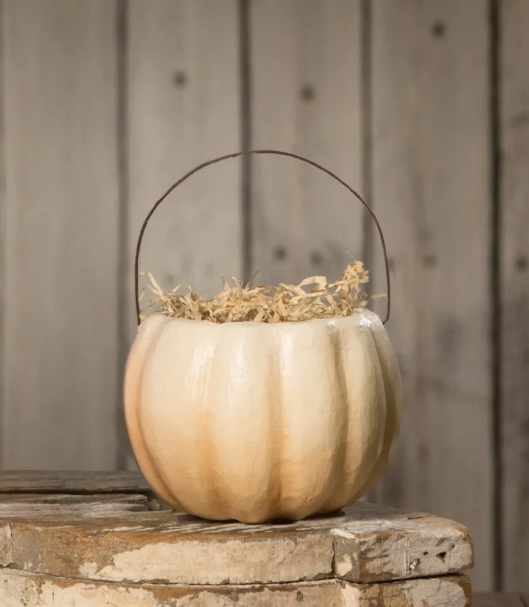 20 Halloween Decor FINDS That Are Actually Chic - 9 A cream-colored pumpkin-shaped container filled with straw sits on a weathered wooden surface against a rustic wooden background, making it a charming addition to your Halloween decor.