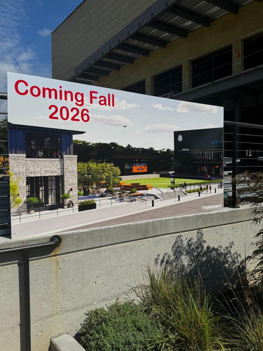 The Commons: Lexington’s Next Big Gathering Space - 2 A sign displays a rendering of a future building and courtyard in Lexington, with large red text reading “Coming Fall 2026.” The design hints at a vibrant gathering place to be known as The Commons.