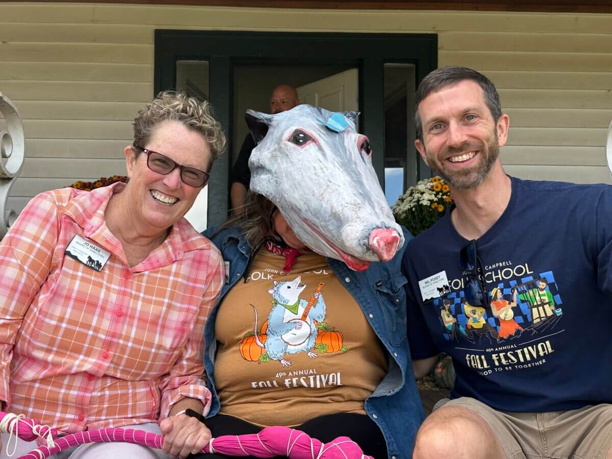 She's Making the Blind Feel Seen Through Louisville’s Newest Museum Experience - 4 Photograph of two smiling adults posing with a person wearing white animal mascot. One person wears a red plaid shirt, another wears a dark graphic T-shirt, and the person wearing the animal mask sits between them near a doorway.