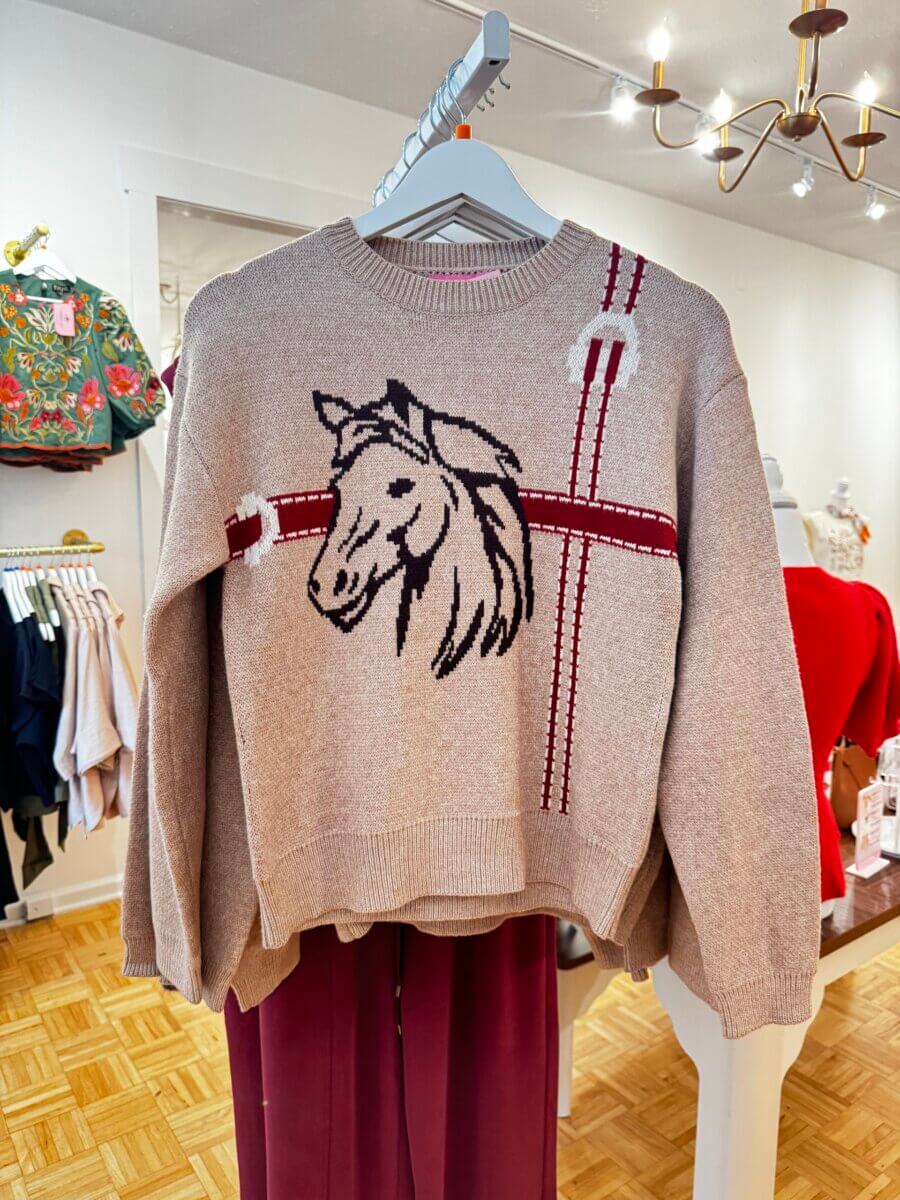 17 Louisville FINDS for October: Fall Fashion, Festive Decor & Game-Day Essentials - 4 Beige sweater with a black outlined horse head design and red and white plaid accents, displayed on a hanger in a clothing store—one of our favorite FINDS from Louisville this October.
