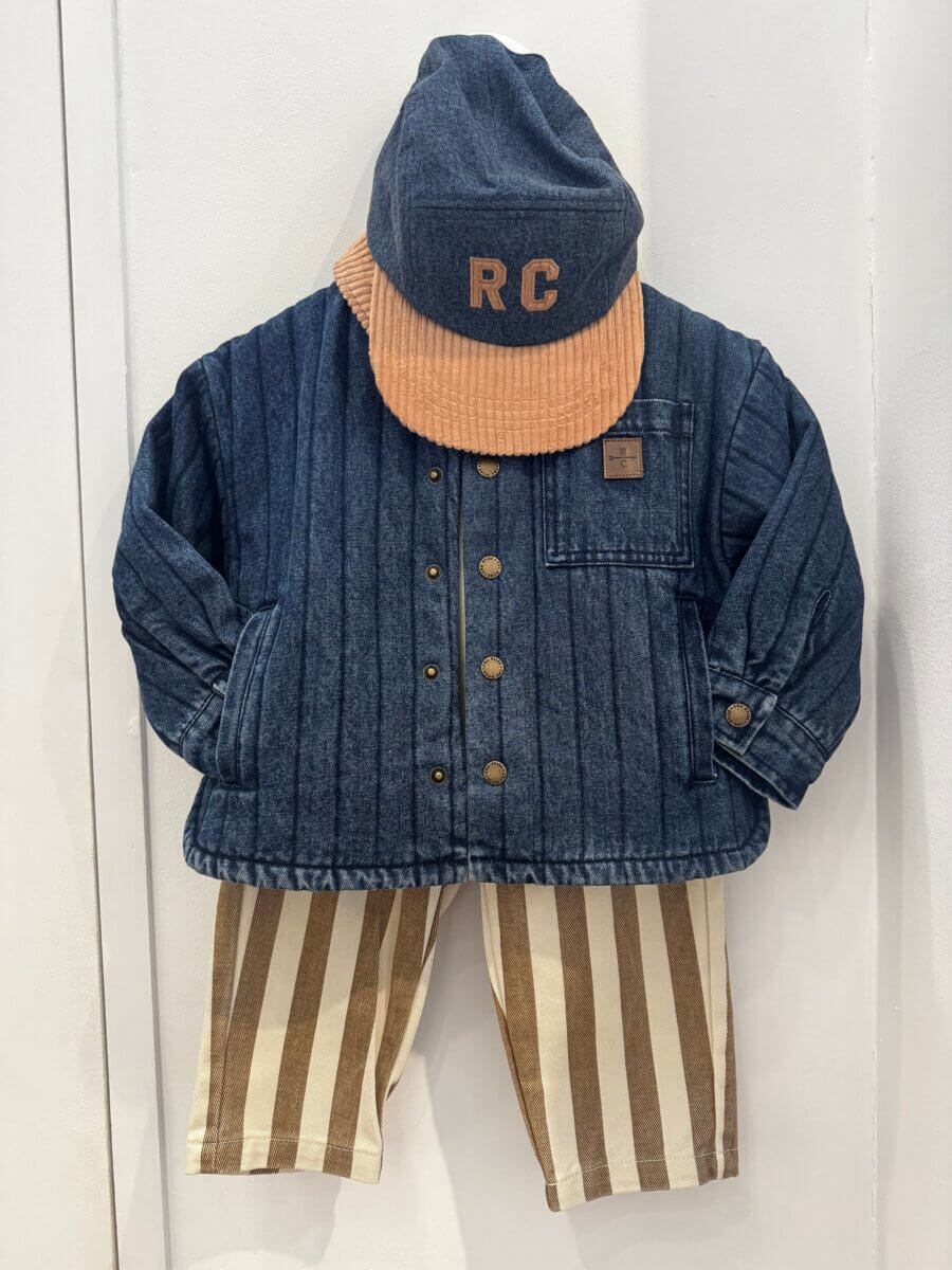 17 Louisville FINDS for October: Fall Fashion, Festive Decor & Game-Day Essentials - 16 Children’s outfit displayed on a wall, featuring a blue quilted jacket, brown and white striped pants, and a blue cap with brown brim and “RC” initials—a charming October FINDS for any Louisville youngster.