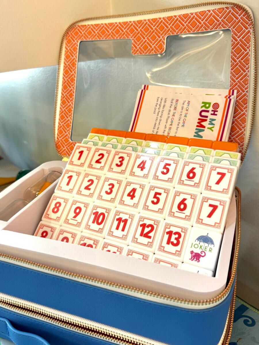 17 Louisville FINDS for October: Fall Fashion, Festive Decor & Game-Day Essentials - 10 A blue zippered case contains Rummikub tiles, scorecards, and a Joker tile, with a clear lid displaying the contents—an exciting Louisville FINDS discovery perfect for game nights in October.