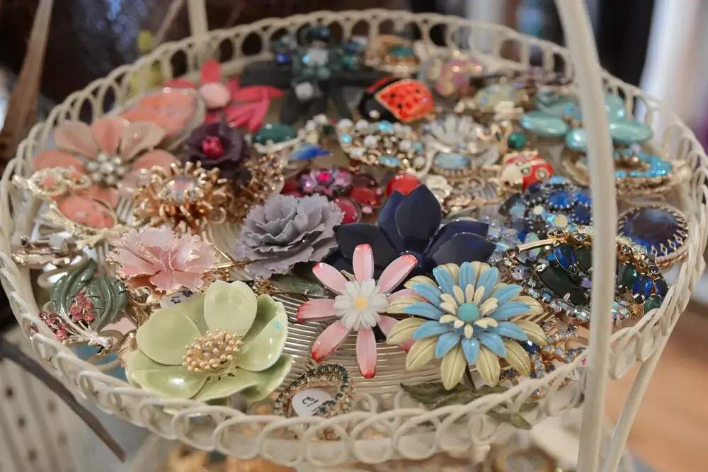 Louisville Fall Fashion 2026: 3 Runway Trends to Incorporate - 3 A white metal basket filled with various colorful, flower-shaped brooches and pins arranged closely together—perfect for embracing Fall Fashion 2026 runway trends.