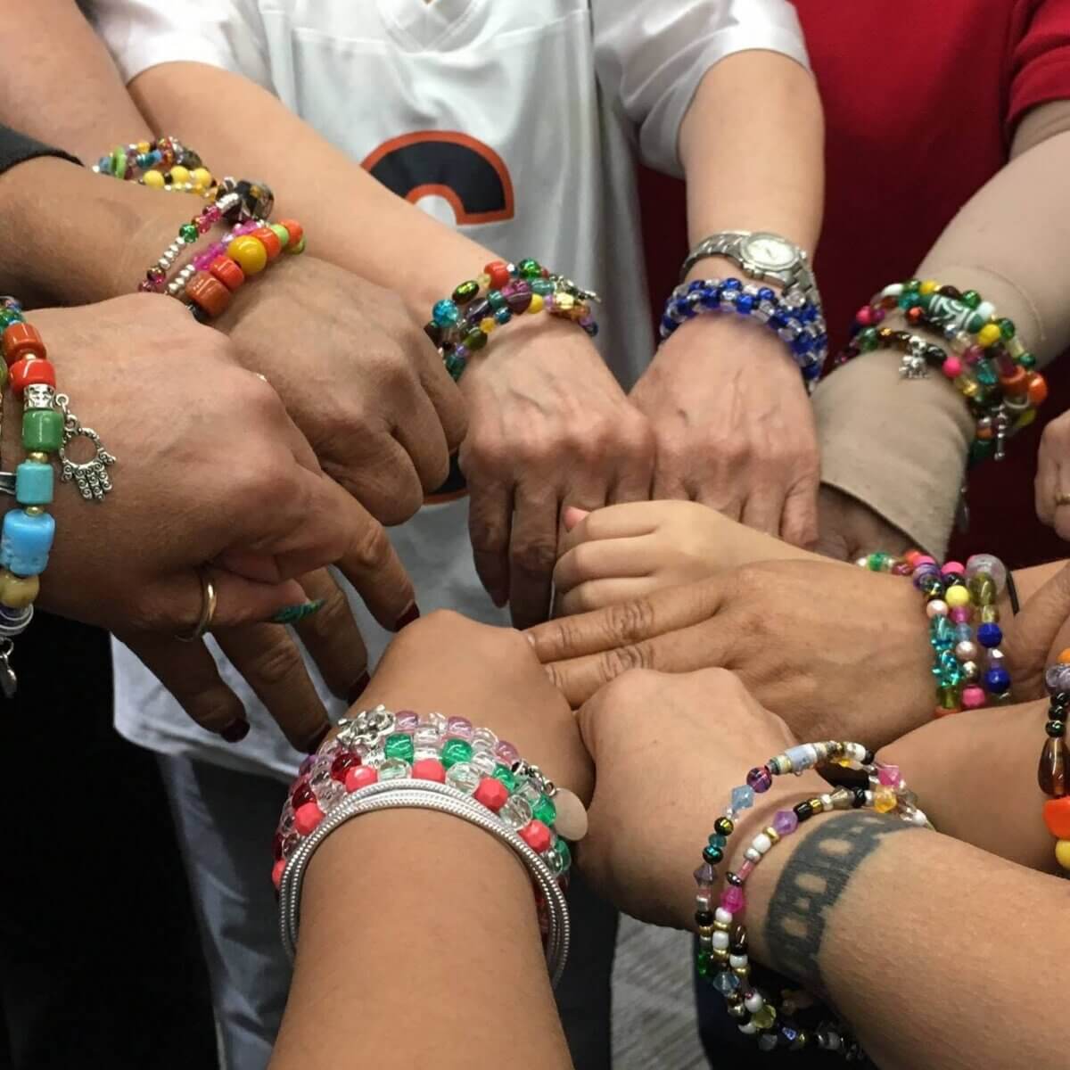 Breast Cancer Sucks. 6 Surprising Ways to Support Survivors - 6 A group of people join hands in a circle, each wearing colorful beaded bracelets, showing their unity and support for breast cancer survivors.