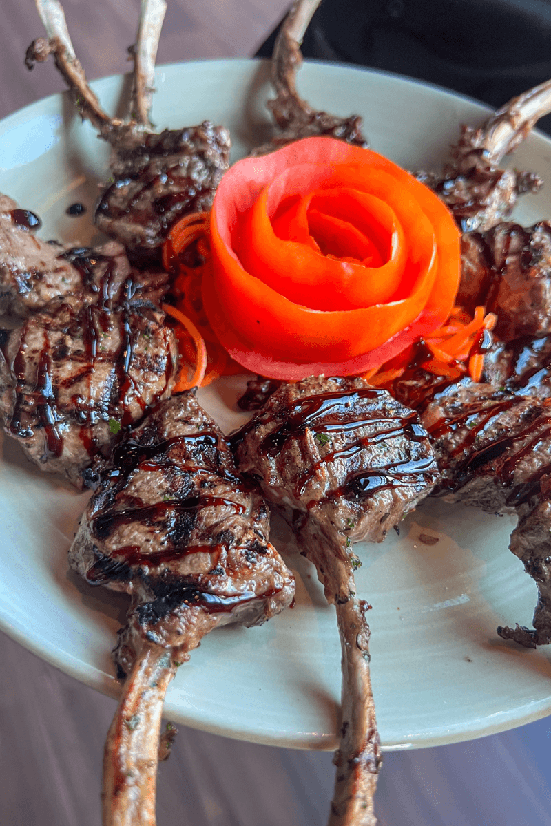 Did You Know You Could Spend the Night in the Memphis Pyramid? - 5 Grilled lamb chops drizzled with sauce, arranged around a tomato rose garnish on a white plate.
