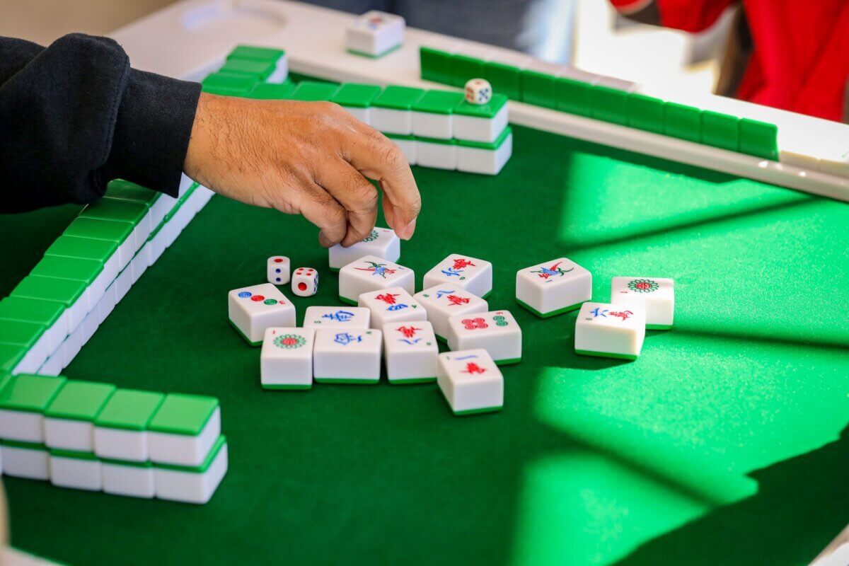 Your Ultimate Memphis Mahjong Guide - 5 A person arranges mahjong tiles on a green table while holding a tile, skillfully following a guide; two dice are also on the table.