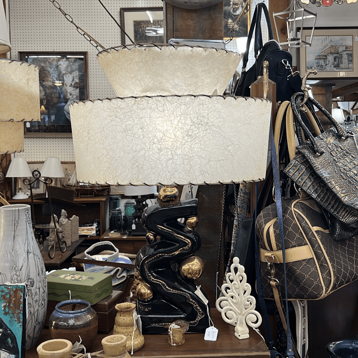 Your Guide to Antiquing in Memphis: 10 Shops Worth Exploring - 4 Large vintage lamp with textured cream shade and black ceramic base with gold accents, surrounded by purses, vases, and decorative items in an antique shop display.