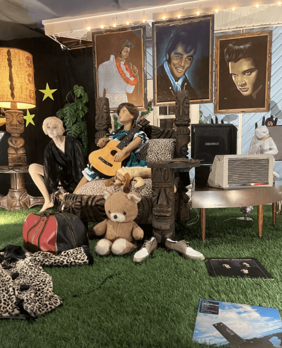 Your Guide to Antiquing in Memphis: 10 Shops Worth Exploring - 2 Eclectic room with three Elvis Presley portraits, mannequins, a guitar, teddy bear, vintage radio, lamp, records, and a large red duffle bag on artificial grass.