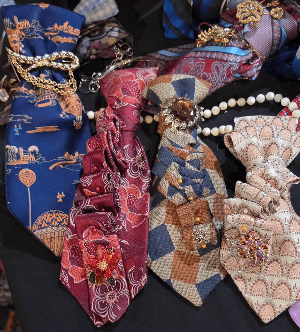 Your Guide to Antiquing in Memphis: 10 Shops Worth Exploring - 7 Four ornate neckties with ruffles, brooches, and jewelry accents are displayed on a black surface, featuring various patterns and embellishments.