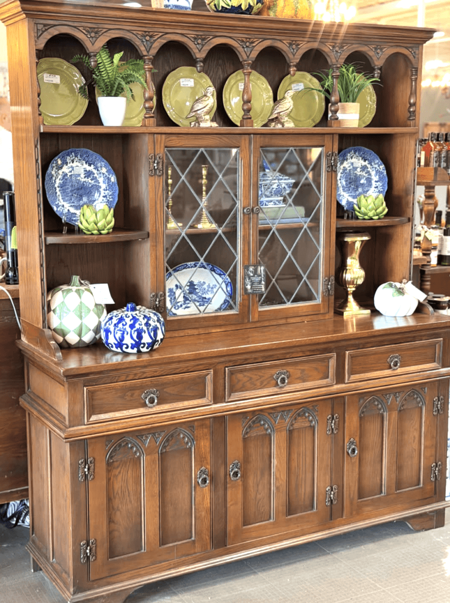 Your Guide to Antiquing in Memphis: 10 Shops Worth Exploring - 9 Wooden hutch with glass-paneled doors displays blue and green ceramic plates, bowls, and decorative items, including a gold vase and green artichoke sculptures.