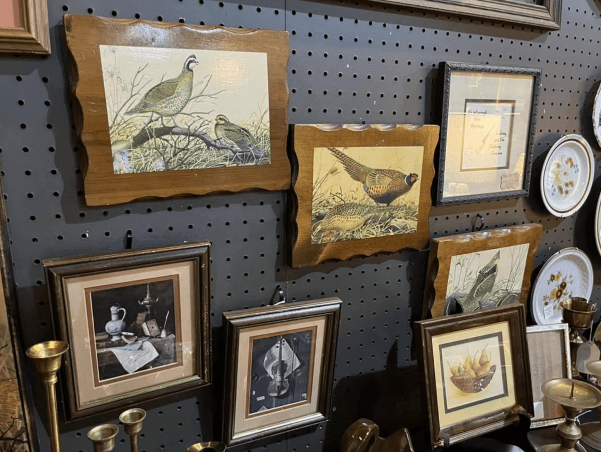 Your Guide to Antiquing in Memphis: 10 Shops Worth Exploring - 8 Framed wildlife and still life art prints are displayed on a black pegboard wall, alongside decorative plates and brass candlesticks.