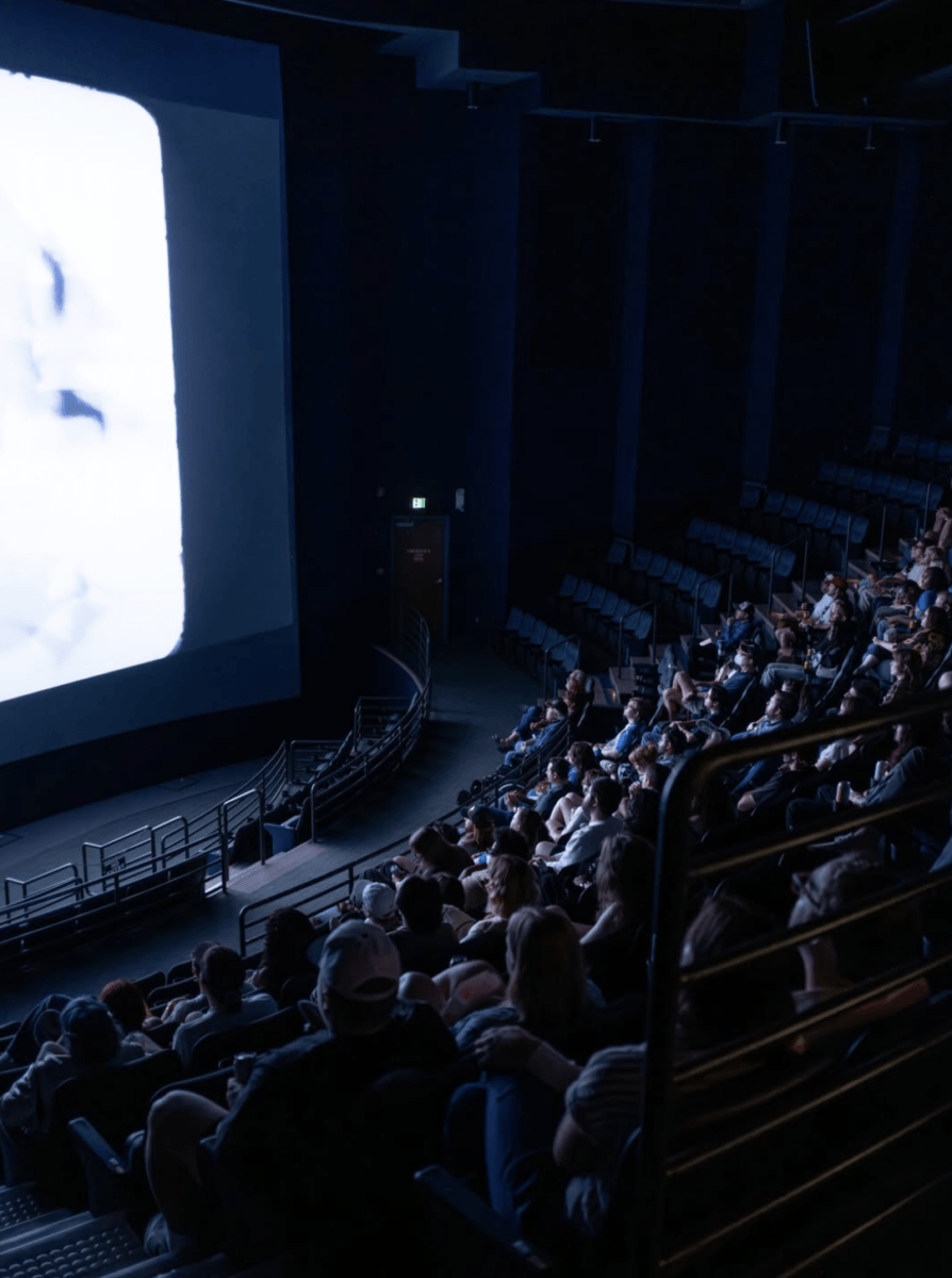 Where to Watch Spooky Movies Under the Stars Around Memphis - 4 Audience seated in a dark theater watching a film on a large screen, with rows of empty seats visible toward the back.