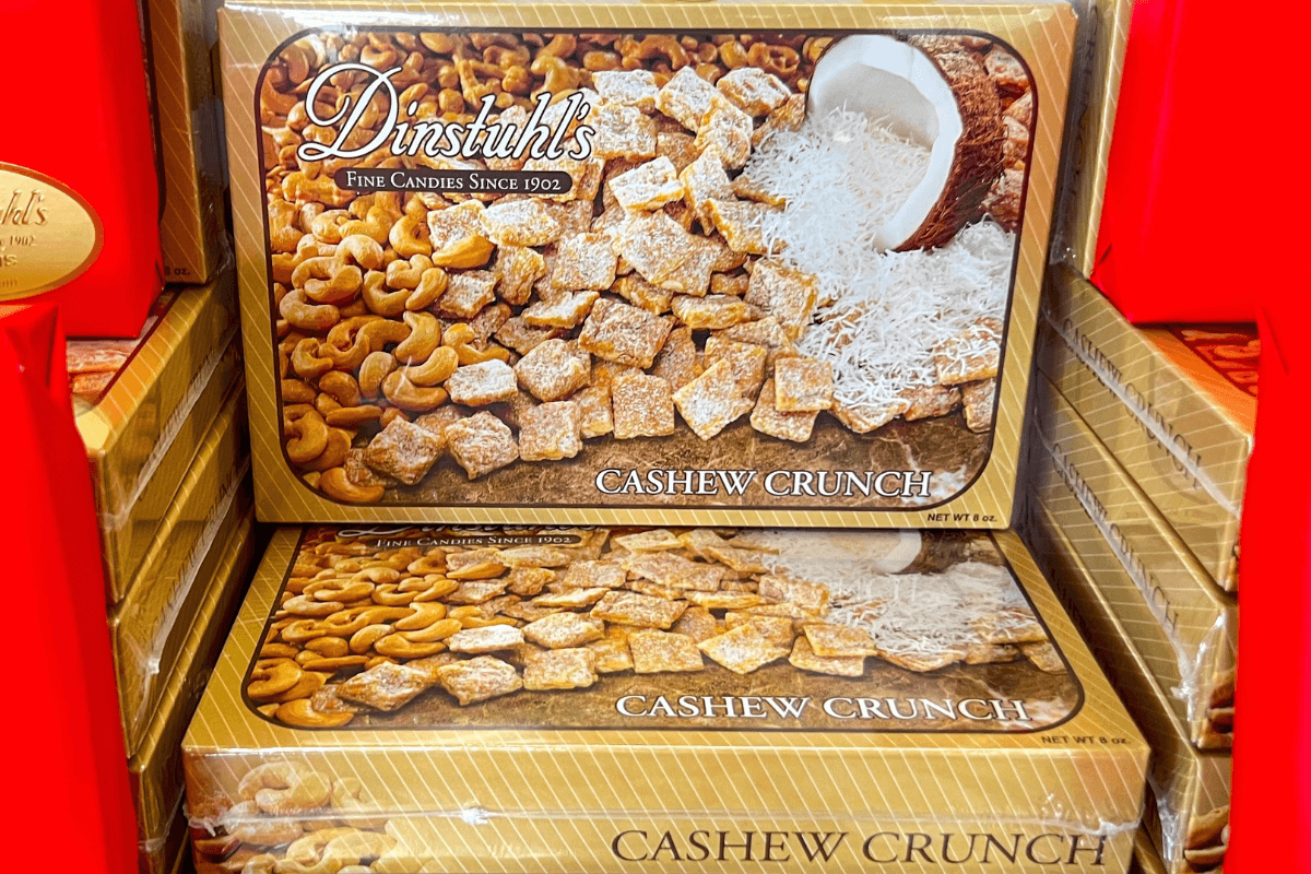 A box of Dinstuhl’s Cashew Crunch candy is displayed, featuring images of cashews, coconut, and coated candy pieces on the packaging.