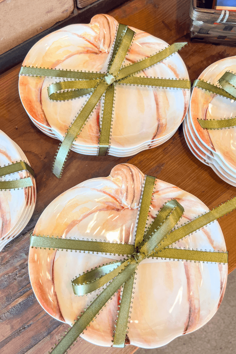 Stacked ceramic pumpkin-shaped plates tied with green ribbon rest on a wooden surface.