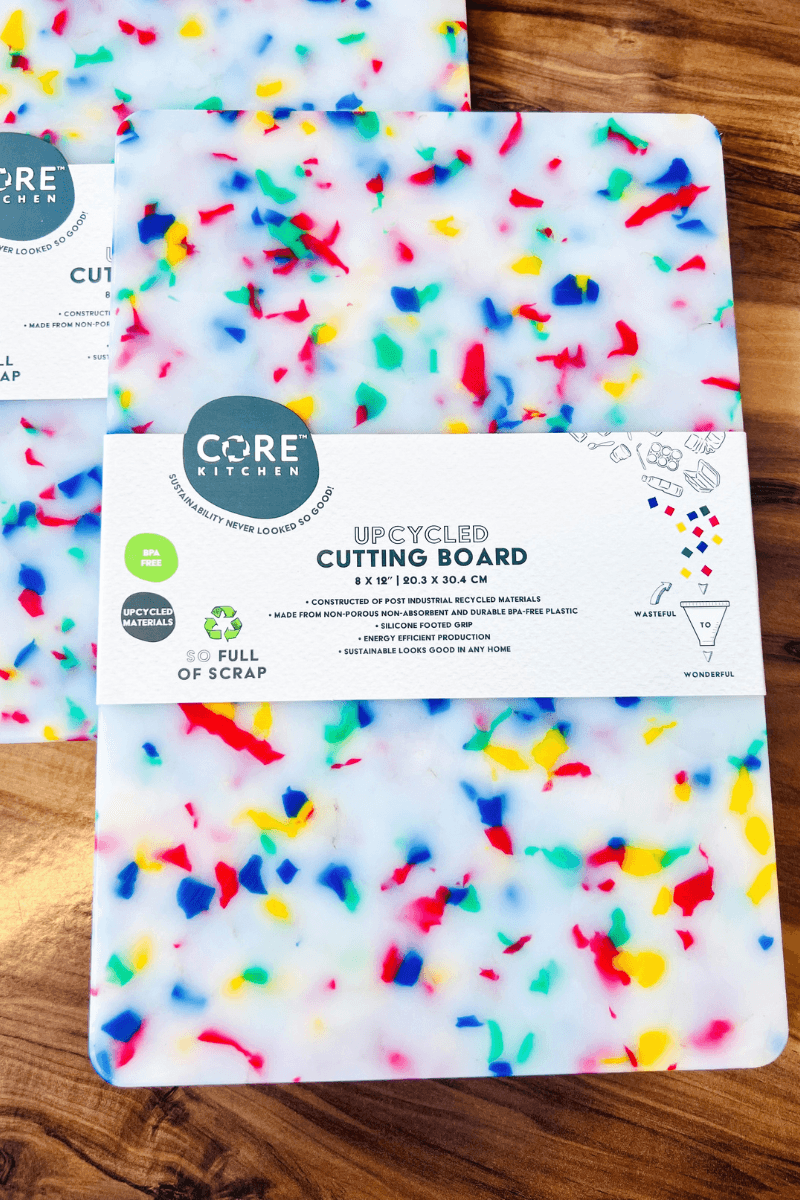 Rectangular Core Kitchen upcycled cutting board with colorful confetti design on a wood surface. Packaging highlights eco-friendly materials and dishwasher safety.