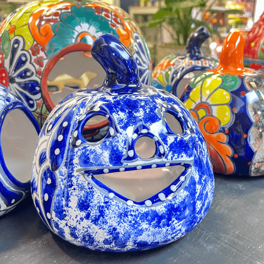 Ceramic pumpkin decorations with colorful, hand-painted designs are displayed on a table, featuring cut-out eyes and smiles.