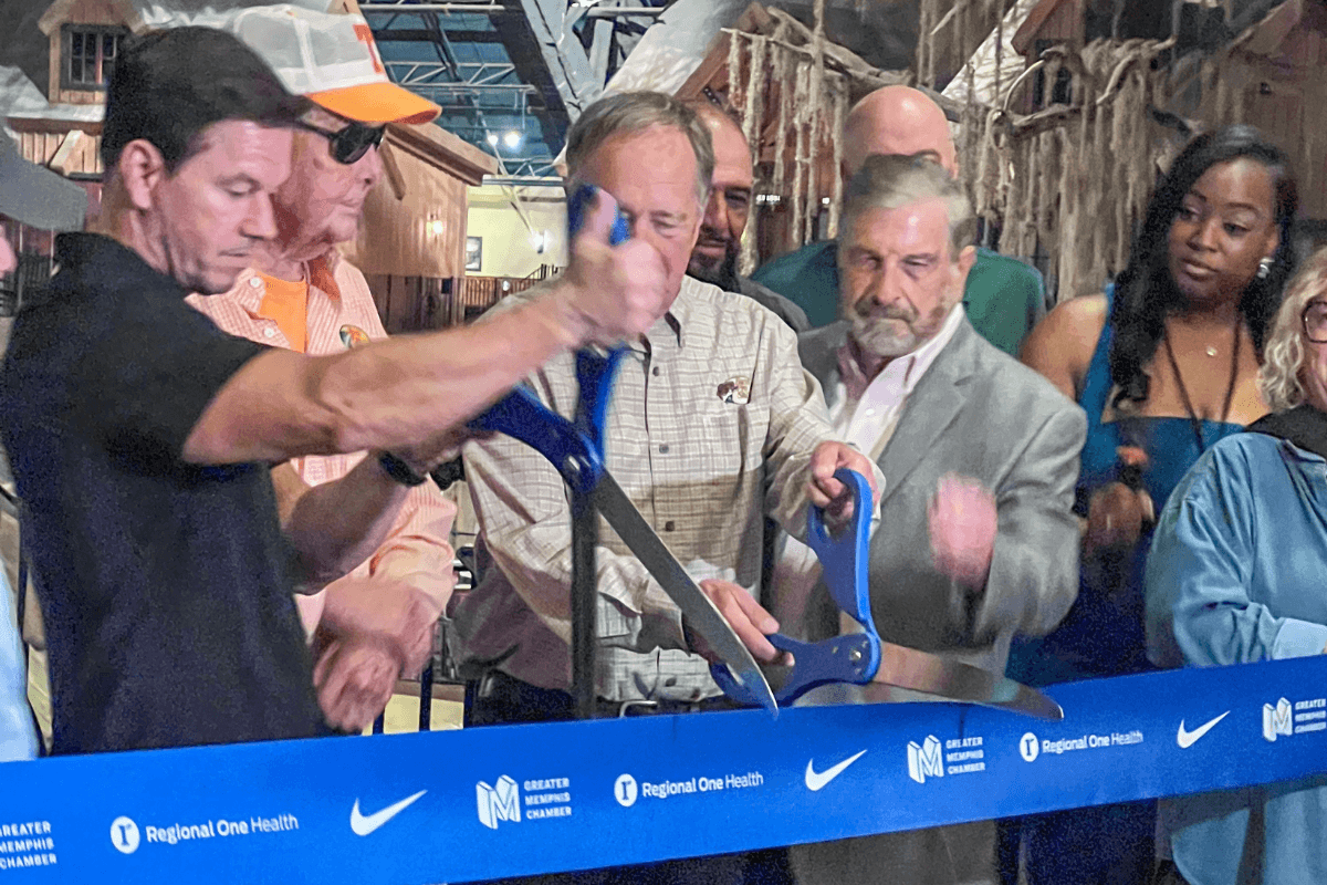 Did You Know You Could Spend the Night in the Memphis Pyramid? - 3 A group of people participates in a ribbon-cutting ceremony, holding large scissors and standing behind a blue ribbon with logos.