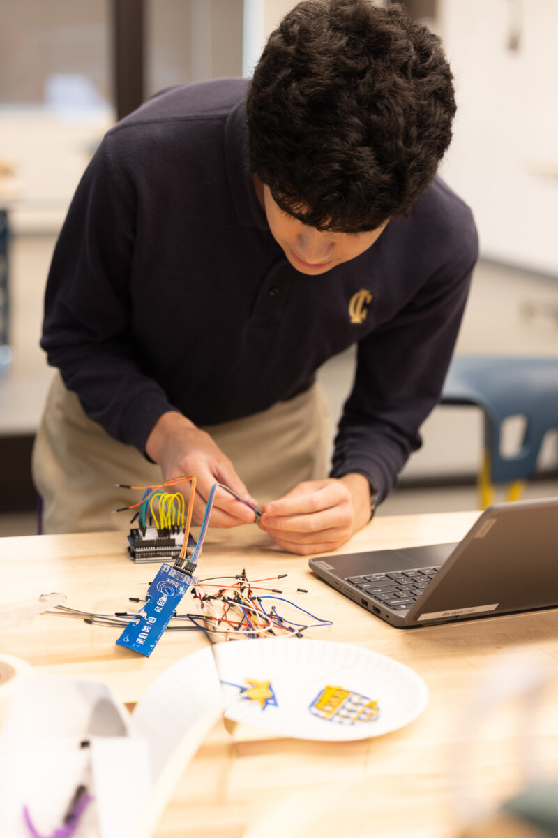 This Nashville School Is Giving Students More Room to Explore, Create & Build - 5 A person assembles electronic components on a table next to a laptop in a classroom or lab setting, where ai learning tools are integrated into their hands-on experiments.