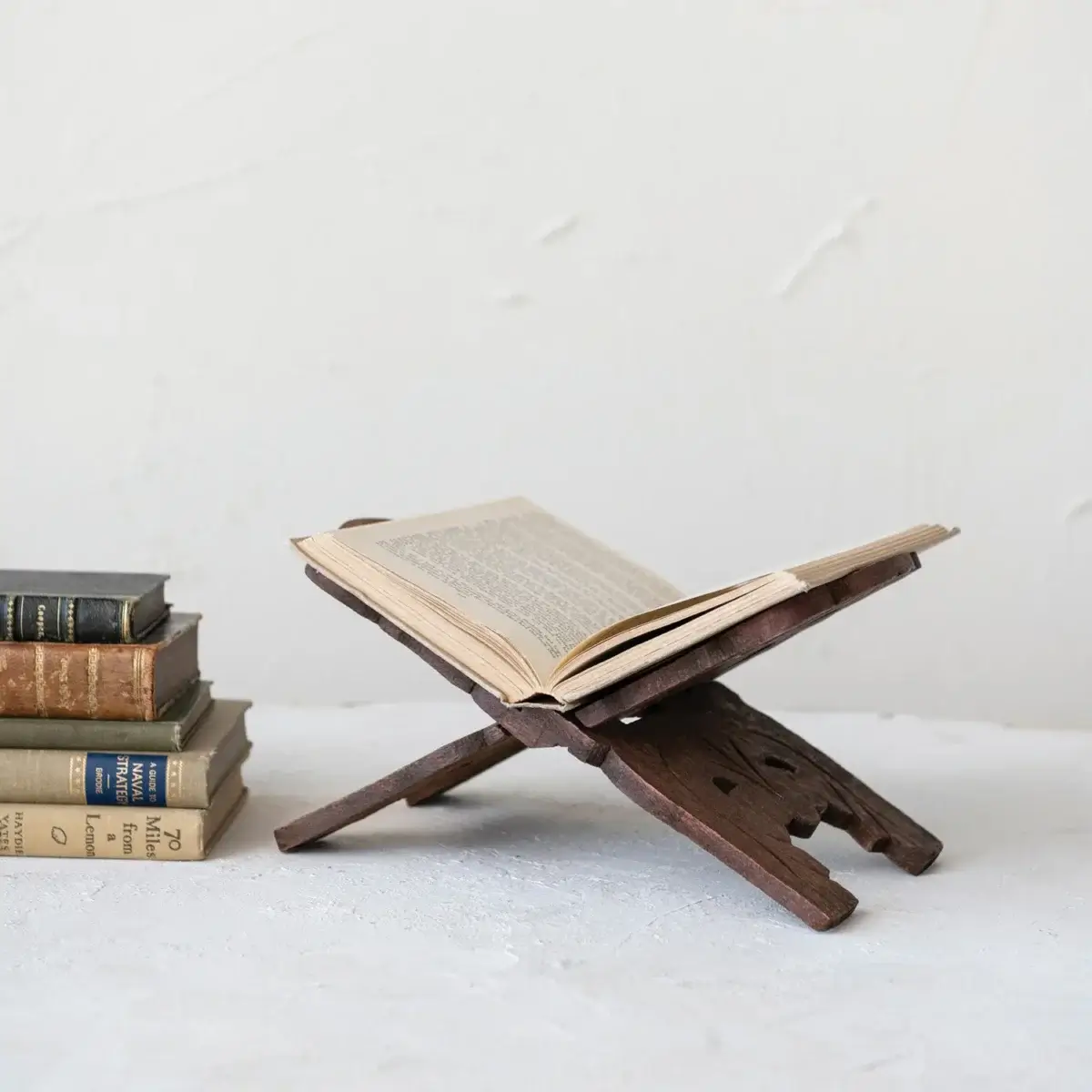 An open book rests on a wooden book stand next to a small stack of closed books on a white surface against a light background, evoking the quiet charm of September FINDS in Nashville.