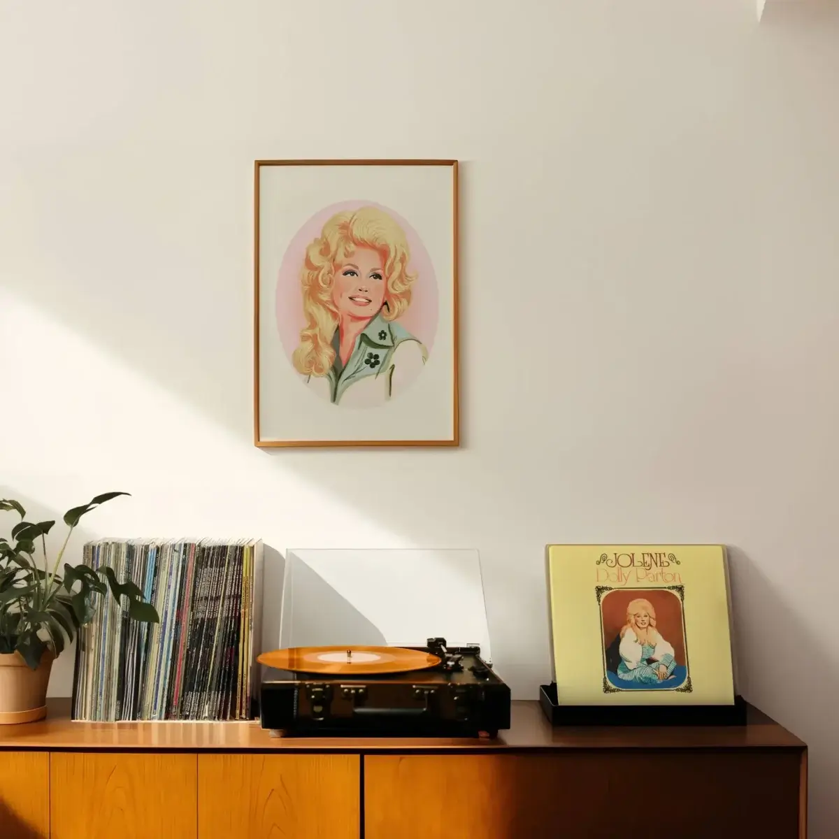 A framed portrait hangs above a wooden sideboard with a plant, vinyl records, a record player, and a vinyl album cover displayed upright.