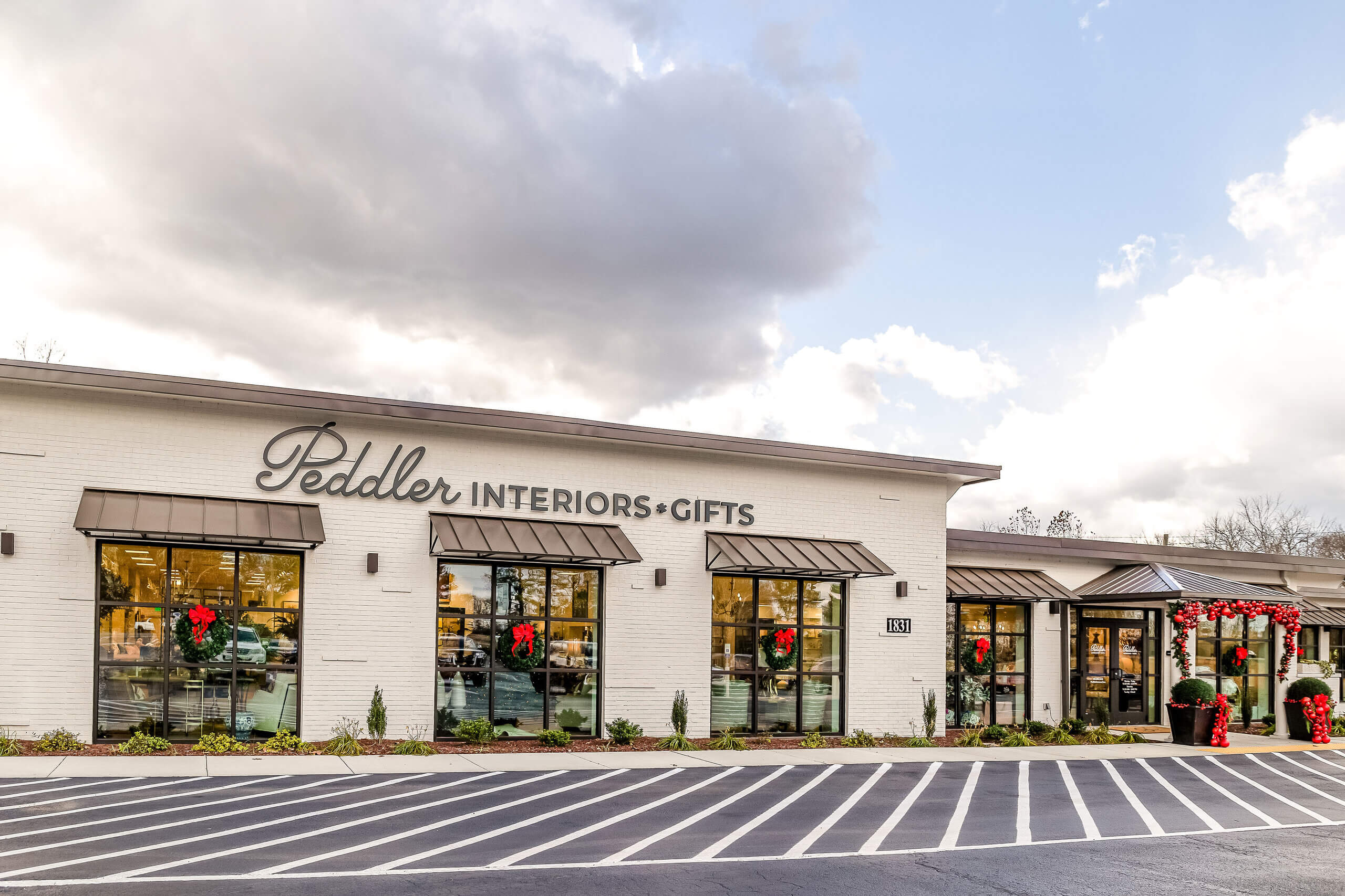 Exterior of Peddler Interiors & Gifts, a shop specializing in home decor with a white brick facade and striped awnings.