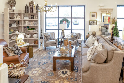 A furniture store showroom featuring a tan sofa, two patterned armchairs, a leather chair, and a shelving unit with interior design home decor.