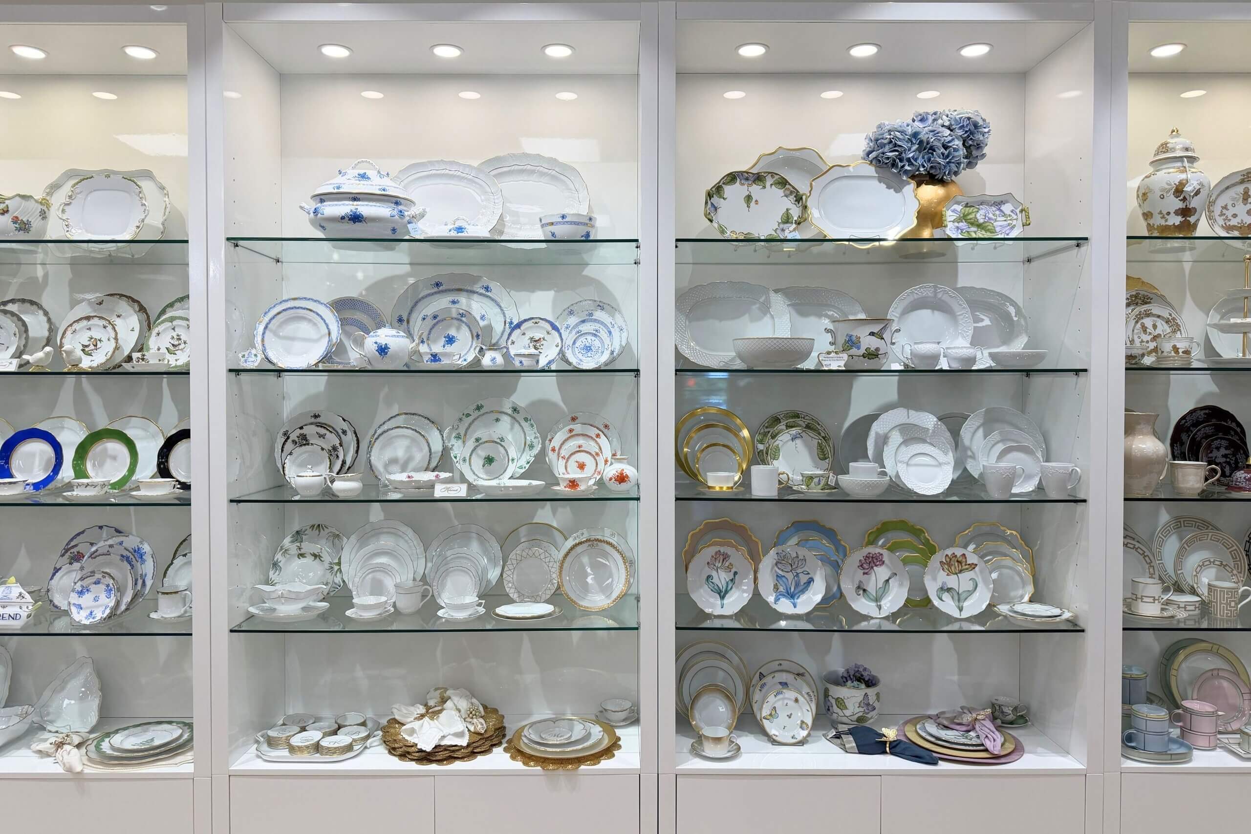 Display cases at Peddler Interiors filled with fine china plates, bowls, teacups, and serving dishes suitable for home gifts.