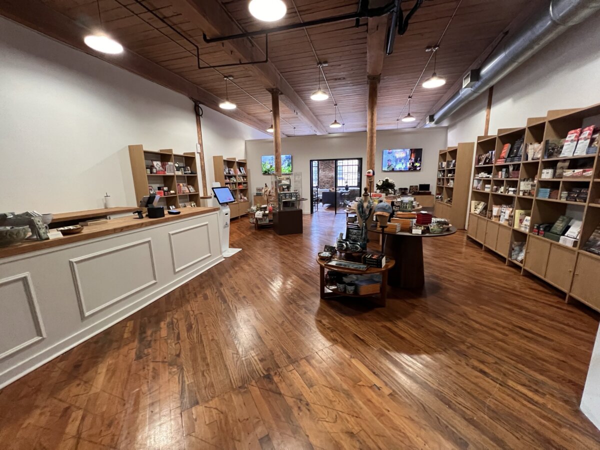 Nashville Steals, Deals & Announcements: October 2026 - 10 A bookstore with wooden floors, shelves of books along the walls, a counter on the left, and a round display table in the center. Natural light comes through glass doors at the back.