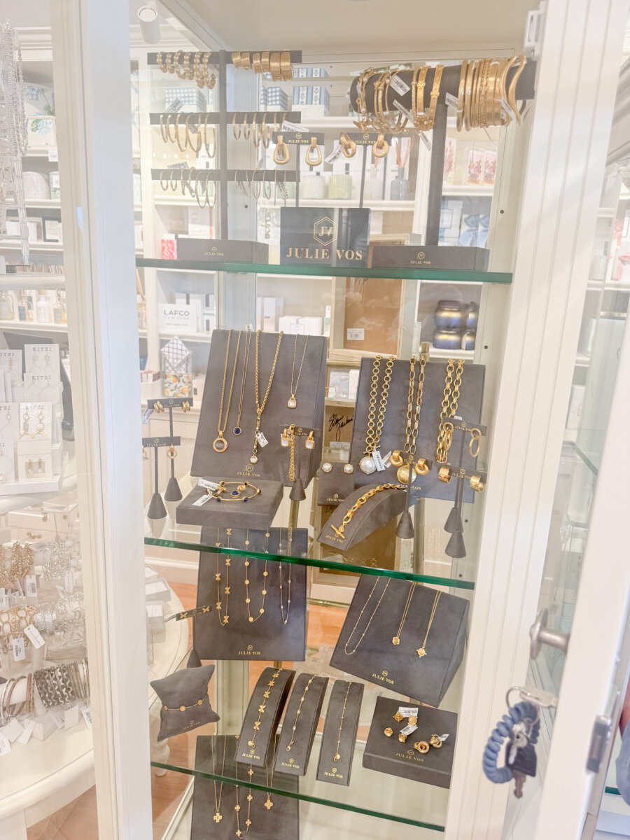 Nashville Steals, Deals & Announcements: October 2026 - 11 Glass display case containing various gold jewelry pieces, including necklaces, bracelets, earrings, and rings, all arranged on black stands and shelves with “Julie Vos” signage visible.