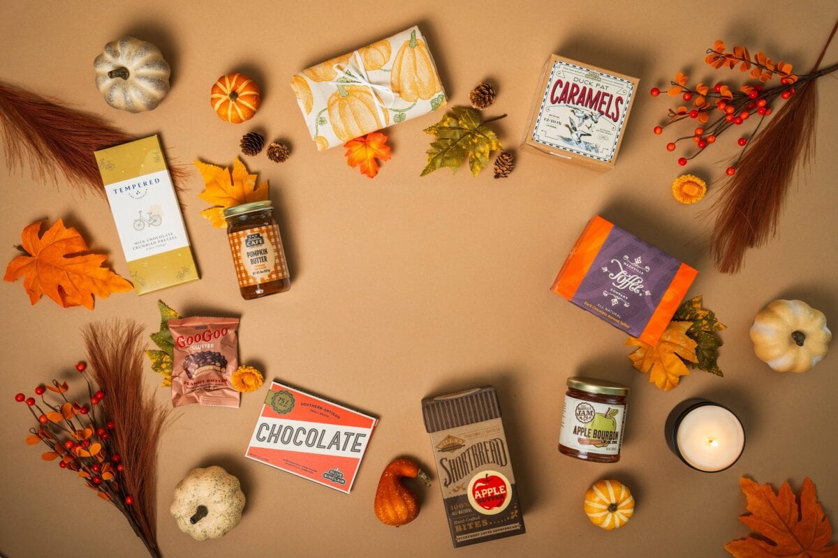 Nashville Steals, Deals & Announcements: October 2026 - 4 Assorted autumn-themed snacks and treats arranged in a circle on a brown background with fall leaves, mini pumpkins, and a lit candle—perfect for celebrating October 2026.