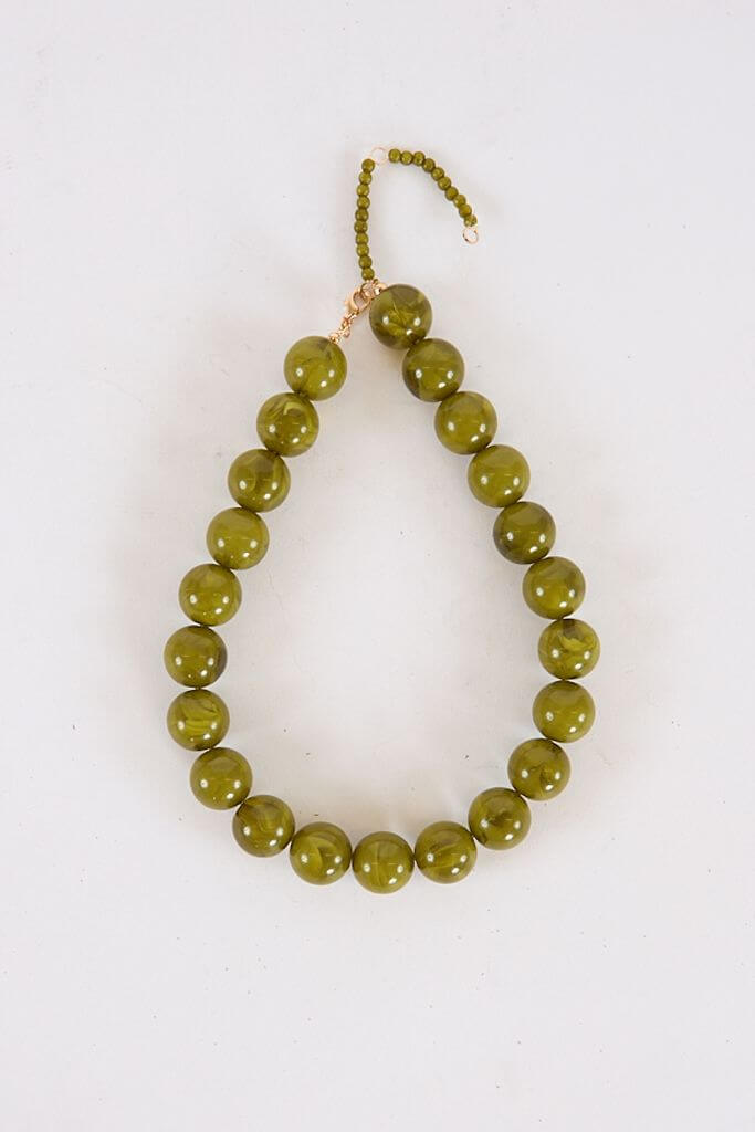 A beaded necklace made of round, shiny olive-green beads with a small adjustable beaded chain and gold clasp, arranged in a teardrop shape on a white background—a stunning September FINDS from Nashville.