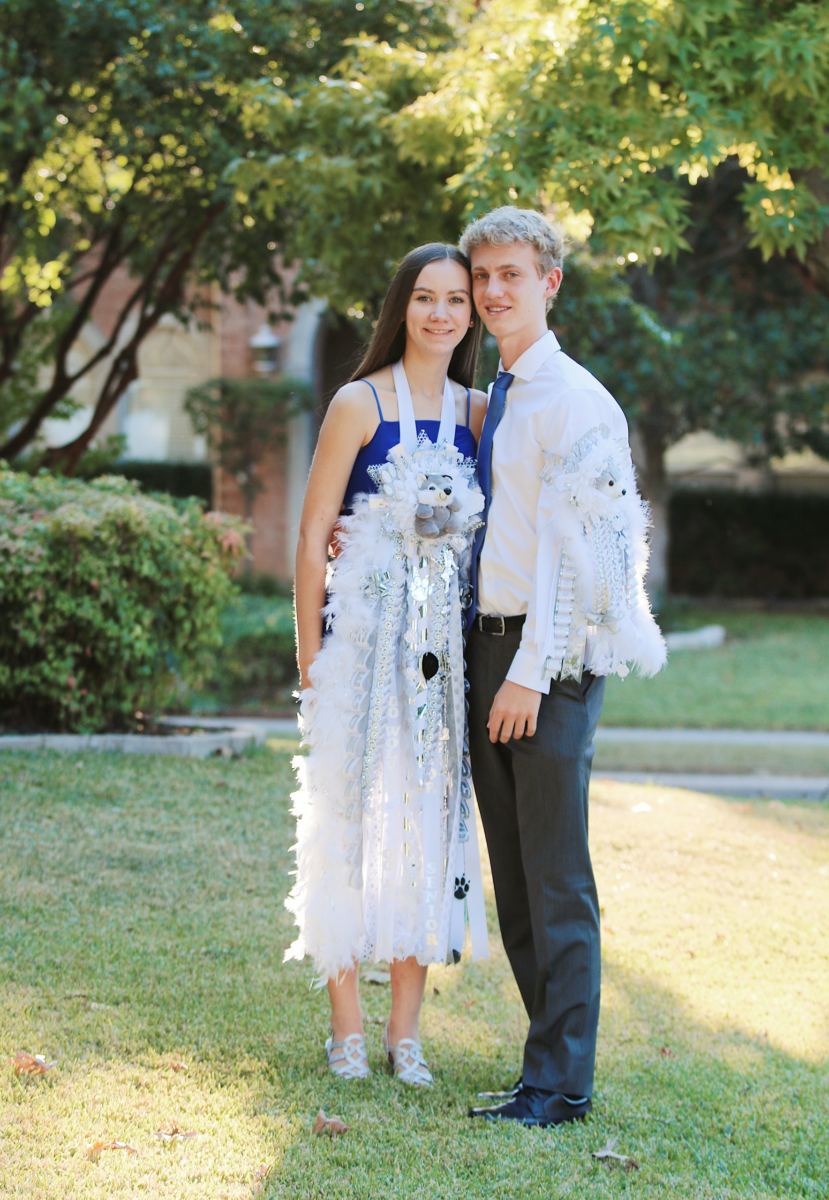 The Bigger the Better! How Texas Homecoming Mums Got So Huge - 5 Two teenagers stand side by side outdoors, dressed in semi-formal attire and wearing large decorative Texas Homecoming Mums with ribbons and trinkets—a beloved Texas tradition that highlights the excitement of homecoming season.