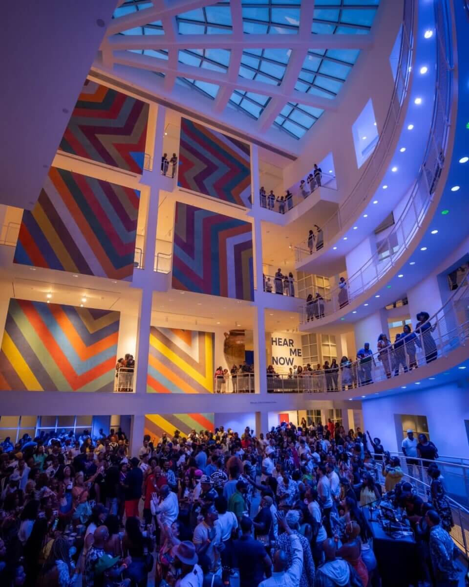 7 Southern Art Museums & Installations Worth Planning a Trip Around - 2 A large crowd gathers inside a modern, brightly lit atrium featuring colorful geometric wall art reminiscent of installations found in renowned Southern Art Museums, with balcony railings on multiple levels.