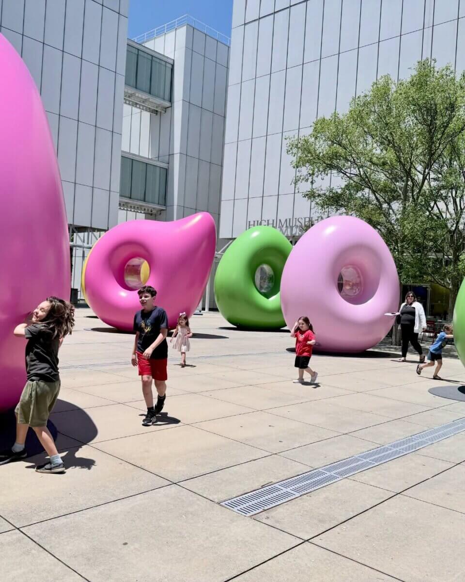7 Southern Art Museums & Installations Worth Planning a Trip Around - 3 Children play around large pink and green abstract art installations, "Los Porfiados," in an outdoor plaza at the High Museum of Art in Atlanta.