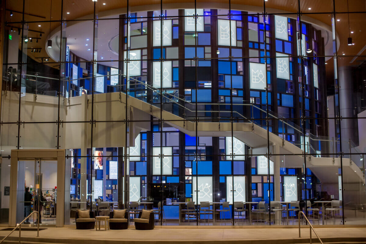 7 Southern Art Museums & Installations Worth Planning a Trip Around - 4 Modern building interior with glass walls, a curved staircase, and a cylindrical structure featuring blue and white illuminated panels with text. Several chairs and tables are arranged in the lobby, creating an inviting space reminiscent of contemporary art installations often found in Southern art museums—perfect inspiration for your next trip planning endeavor.