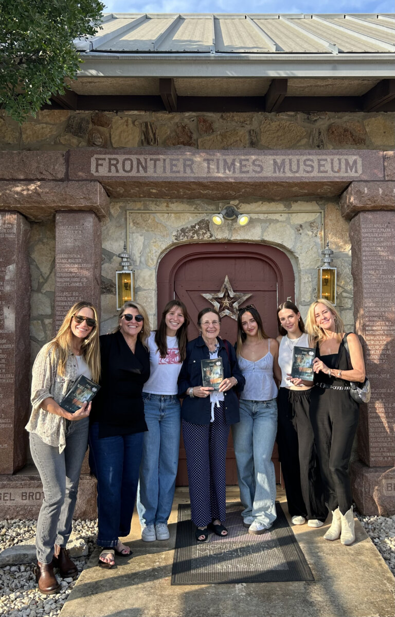 Seven women stand in front of the Frontier Times Museum entrance, posing for a group photo.