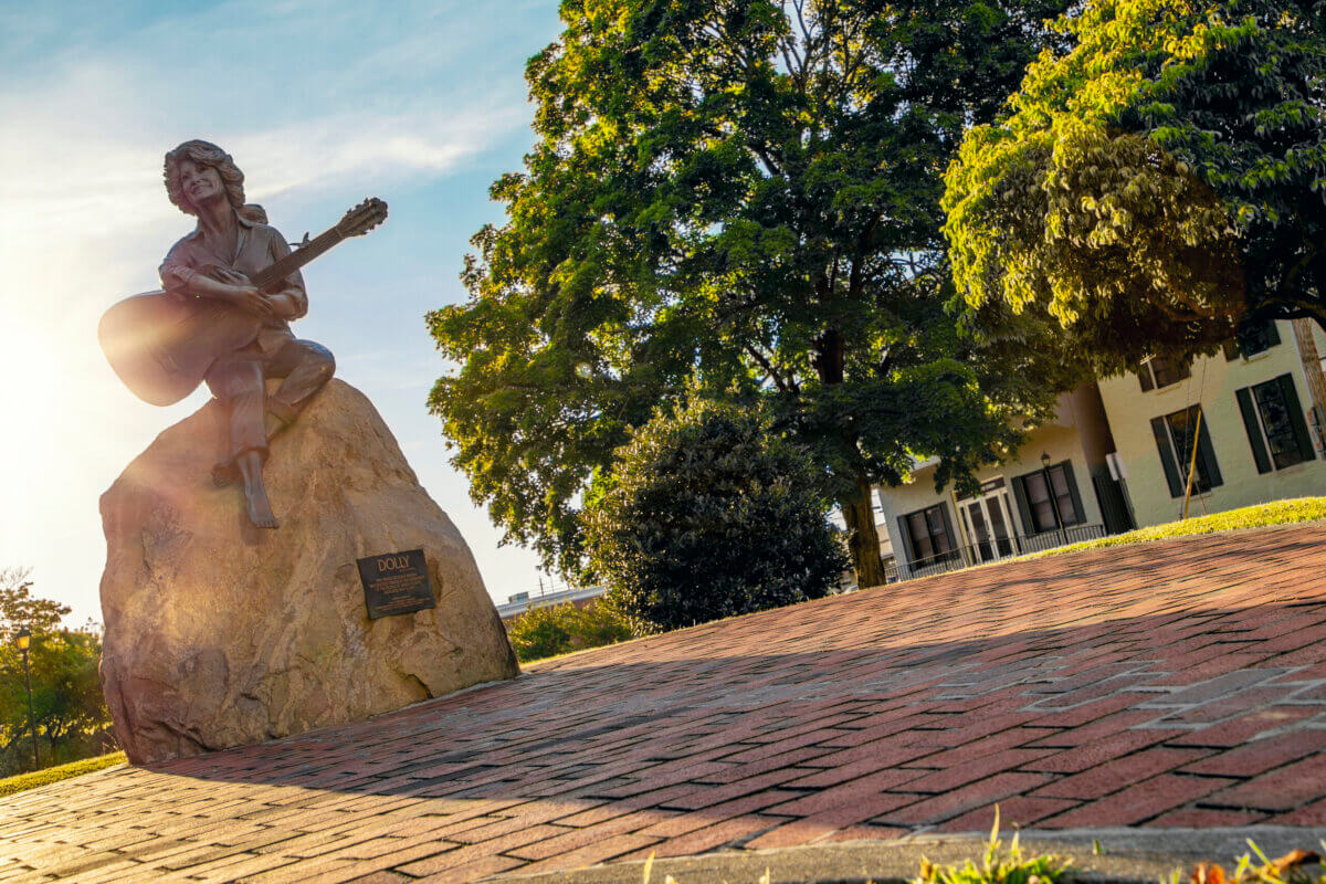 For the Love of Dolly: 7 Ways to Celebrate Her Legacy - 8 Bronze statue of Dolly Parton playing guitar, seated on a rock in Sevierville, Tennessee.