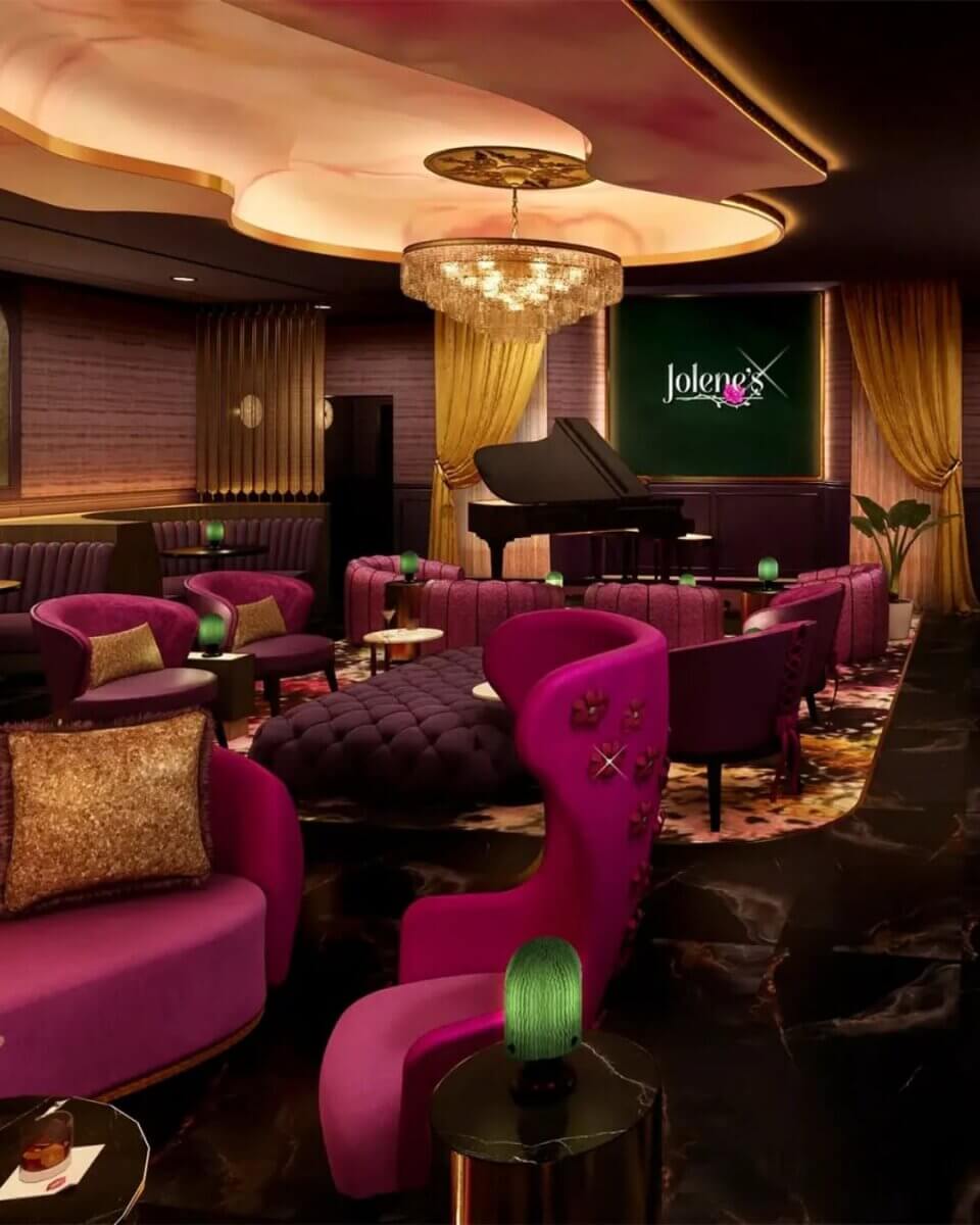 For the Love of Dolly: 7 Ways to Celebrate Her Legacy - 2 Luxurious Jolene's lounge with pink and purple seating, a grand piano on a stage, modern decor, dim lighting, and a Jolene’s sign on the wall at the Songteller Hotel.