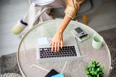 Person working on a laptop at a round white table with a calculator, sticky notes, cup, and potted plant nearby—surrounded by helpful money management tools for better personal finance.