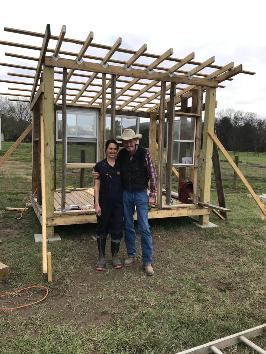 Meet the Lawyer-Turned-Farmer Behind Tennessee’s 5 Porch Farm - 2 Justine Moreau and another individual stand in front of a small wooden structure under construction in a grassy outdoor area, with tools and building materials nearby.