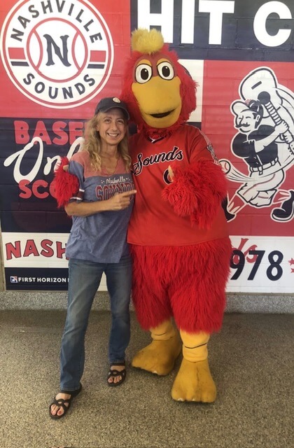 Person posing with the Nashville Sounds baseball team mascot, standing in front of a promotional backdrop for the team, alongside Molly Reed from Nashville Cat Rescue.
