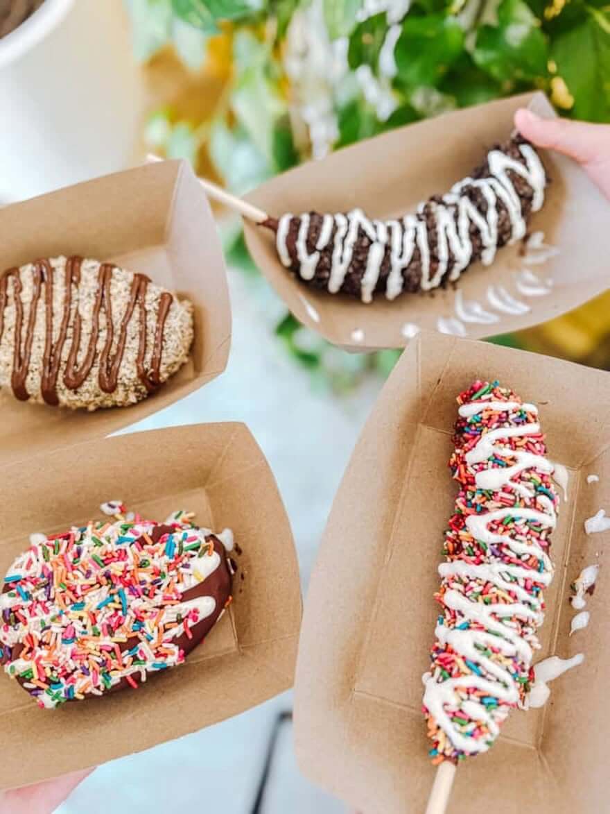 12 New Nashville Restaurants to Try This Month - 9 Four chocolate-covered frozen bananas on sticks, each topped with assorted sprinkles or drizzled chocolate, served in brown paper trays—a delightful treat showing up on the dessert menus of several new restaurants opening in Nashville this September.