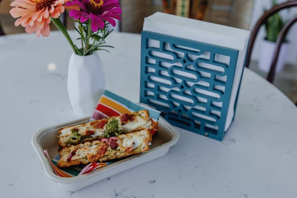 12 New Nashville Restaurants to Try This Month - 3 Two pieces of toasted bread with melted cheese and toppings on a tray, next to a napkin holder and a vase with flowers on a white marble table—perfect for discovering at the new restaurants opening this September among the vibrant Nashville restaurants scene.